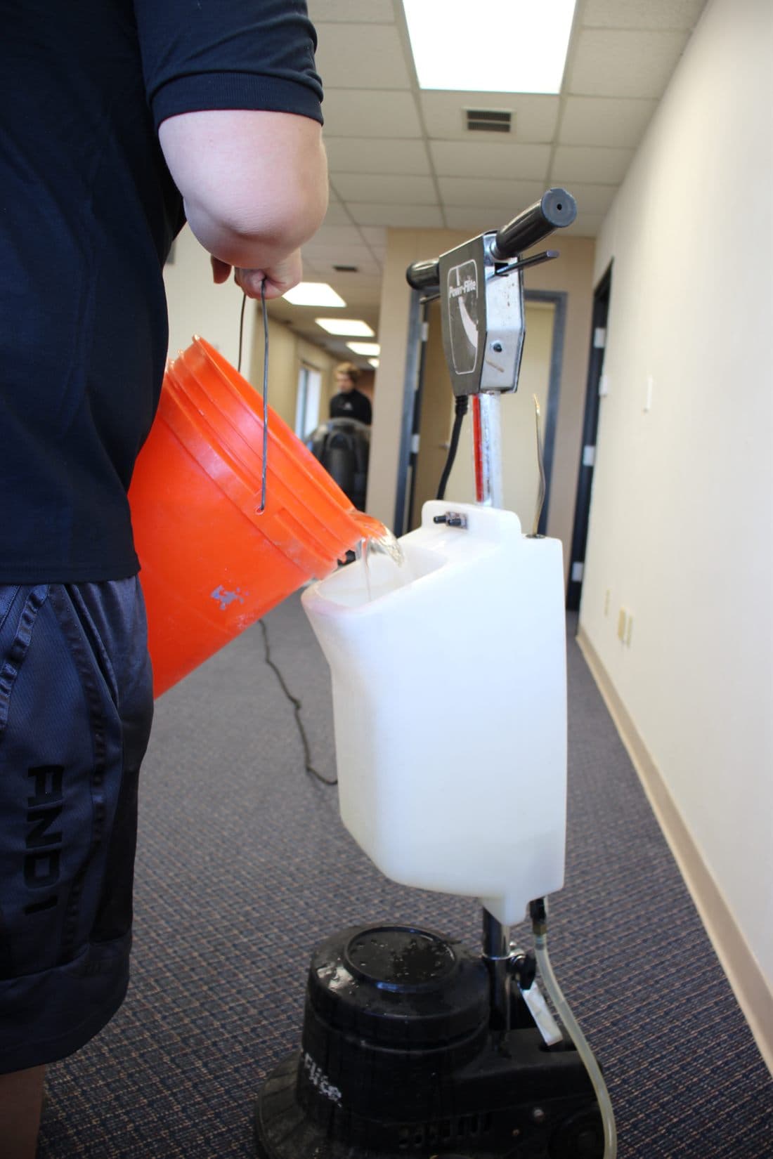 A crew member measuring cleaning solution into a machine's tank.