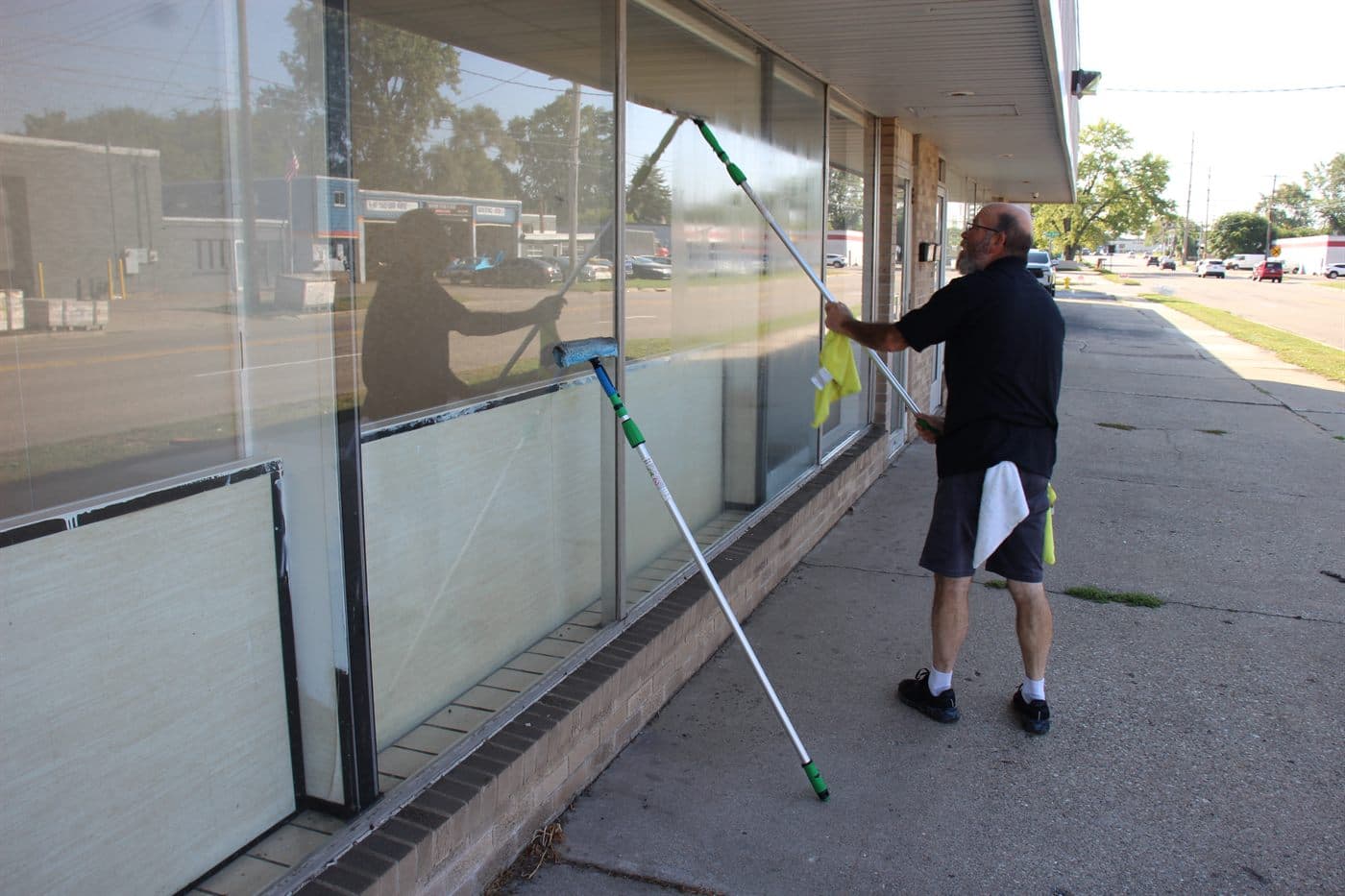 A cleaner working on a storefront's exterior glass with a squeegee and pole.